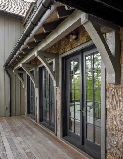 A wooden deck with a wooden railing and large windows.