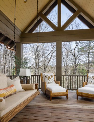 A wooden porch with wicker furniture and a swing.