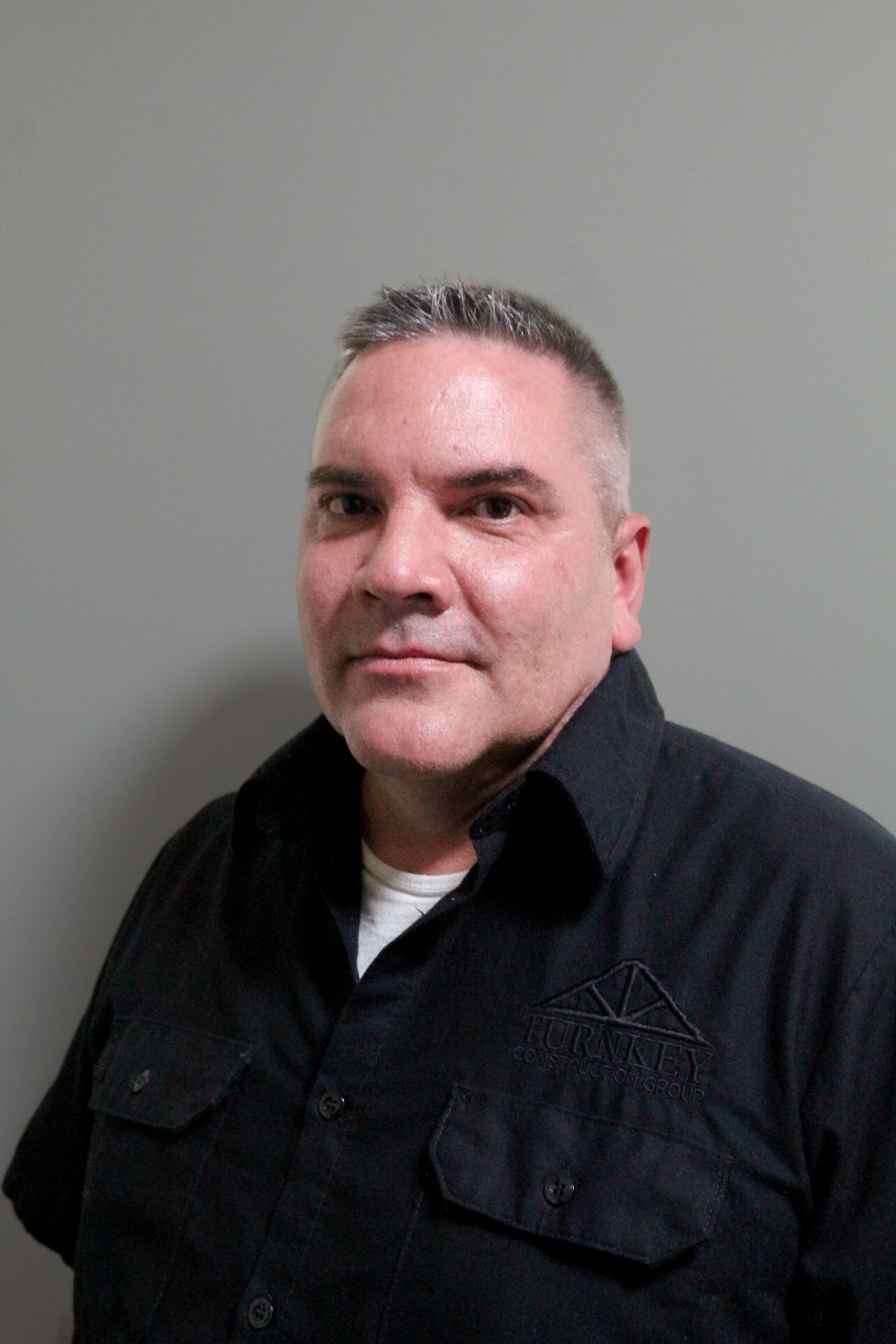 A man in a black shirt standing in front of a gray wall.